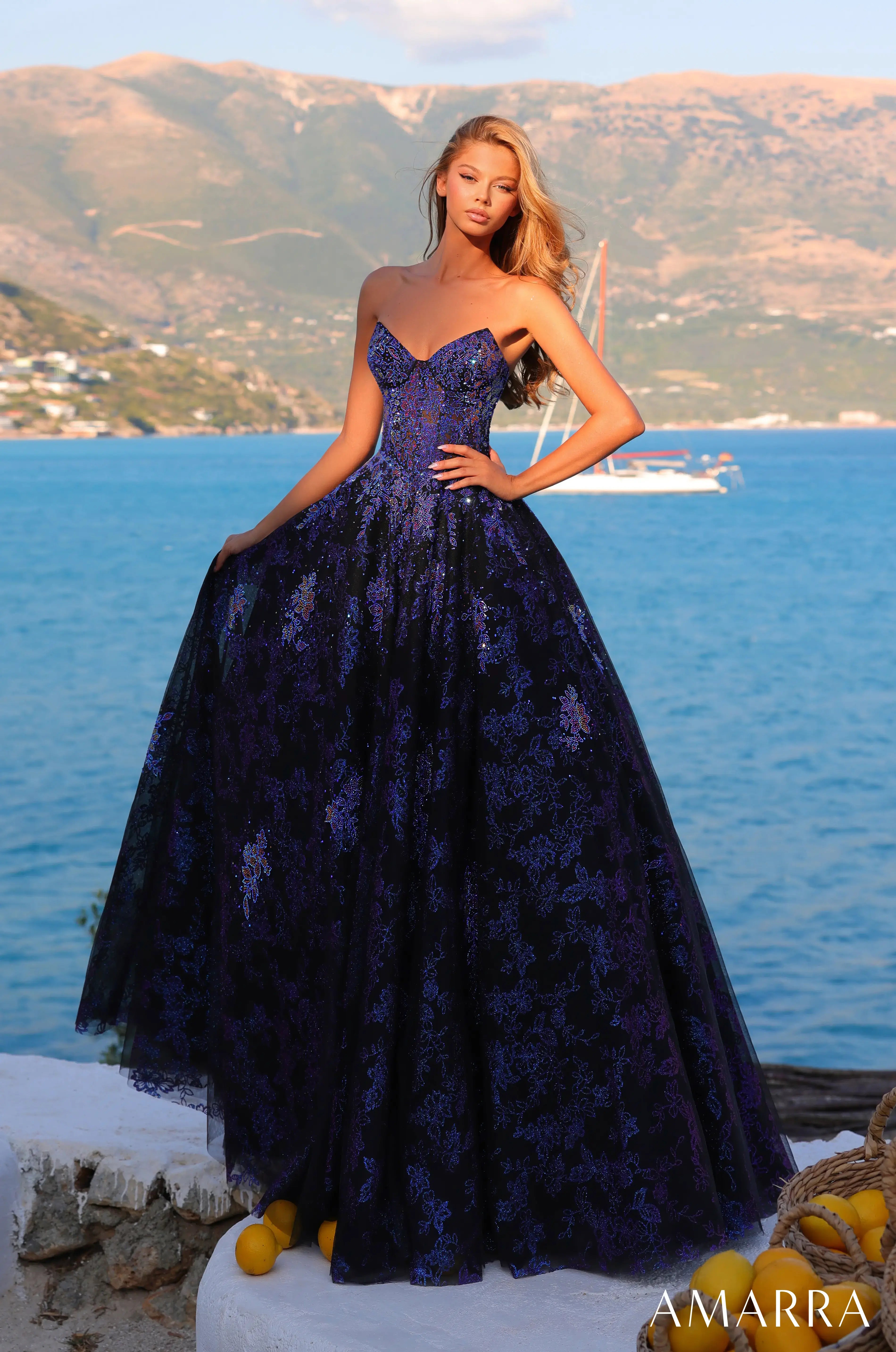 Woman in a purple evening gown standing by a scenic coastal area with 'AMARRA' branding.