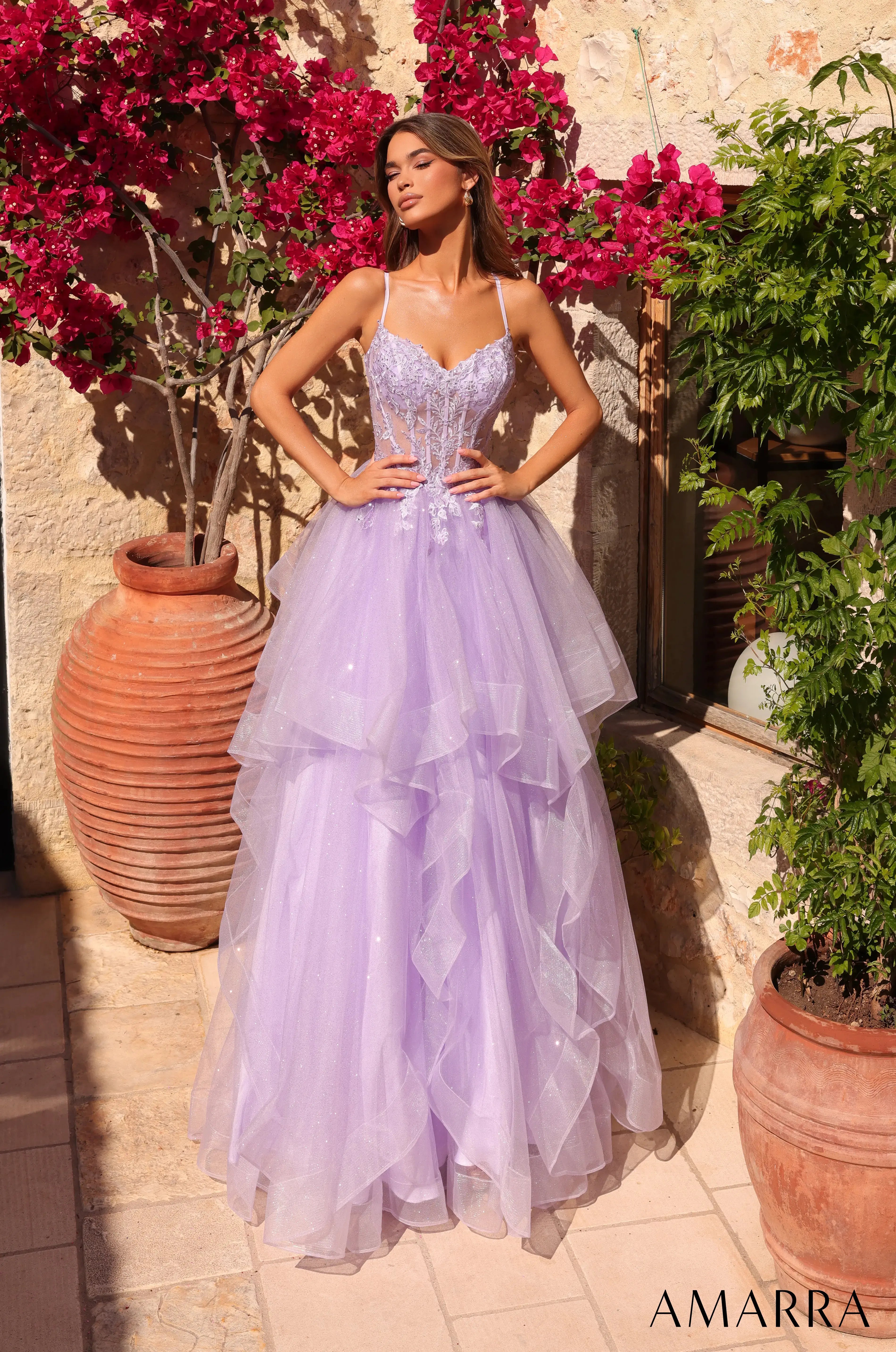 Woman in a lavender gown standing outdoors with flowers and plants around.